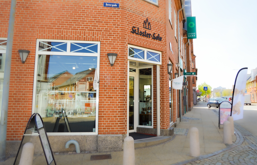 et billede af butikken ude fra idag, med røde mursten og dejlig vejr